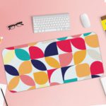 Infidu Artistic Desk Mat with a colorful geometric pattern of overlapping circles and quarter-circles in navy, pink, orange, teal, and yellow. Desk Pad with Keyboard and Mouse