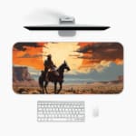 Silhouette of a rider on a horse with a sunset background, featuring dramatic orange and red clouds against a desert-like landscape. A desk pad under the computer