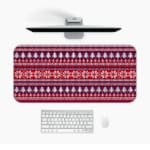 Infidu Desk Pad with a red background, featuring pink, white, and black Christmas trees, reindeer, and snowflakes in a knitted pattern. Design Kept on a computer table