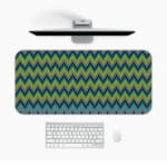 Infidu Desk Pad with a blue background featuring a zigzag knitted pattern in shades of blue, green, and yellow. Design Kept on a computer table