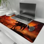 Desk pad featuring a horse rider against a vivid desert sunset with warm colors and rugged rock formations. the desk pad is kept on the laptop