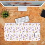 Infidu Boho Pattern Desk Mat with white background and pastel pink and purple dreamcatchers, feathers, and leaf shapes. Desk Pad kept on a orange background