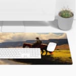 Infidu Horse Rider Desk Pad with a natural landscape showing a person on horseback against mountains, a river, and grassy fields. Desk Pad with Keyboard and Mouse on top of the desk pad