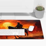 Desk pad featuring a horse rider against a vivid desert sunset with warm colors and rugged rock formations. Desk Pad with Keyboard and Mouse on top of the desk pad