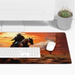 Desk pad with a horse rider against a vivid orange sunset and reddish-brown desert landscape, with dark cliffs and horse in contrasting colors. Desk Pad with Keyboard and Mouse on top of the desk pad