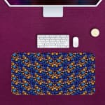 Dark blue desk mat with a dense pattern of small orange and yellow flowers and green leaves, adding vibrant charm to your workspace. Desk Pad on the computer table in pink background