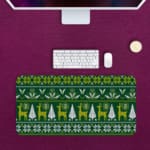 Infidu Knitted Pattern Desk Pad with a dark green background featuring white reindeer, Christmas trees, and snowflakes. Desk Pad kept on a pink background