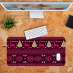 Infidu Desk Pad with a deep purple background and bright pink and white knitted pattern featuring reindeer and trees. Desk Pad kept on a orange background