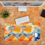 Infidu Desk Pad with an abstract blend of orange, blue, and white, resembling a sunset or colorful sky Desk Pad with Keyboard and Mouse. in orange background