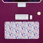 White desk mat with a small, colorful floral pattern featuring purple, pink, and orange flowers with leaves, adding vibrancy to your workspace. Desk Mat with a computer in pink background