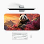 Cute panda on a rock surrounded by pink flowers and a sunset sky with orange, pink, and purple hues. A desk pad under the computer