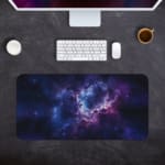 Infidu Space Desk Pad features a nebula scene with rich purples, blues, and a splash of pink, surrounded by stars and cosmic clouds. Desk Pad kept on a gray background