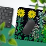 Black desk mat with colorful flower and plant illustrations, including yellow daisies and green plants, featuring a unique design. Desk Pad with Keyboard and Mouse