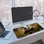 Happy panda with greenery and yellow flowers desk pad, bright and natural design. A computer and laptop are next to the desk pad