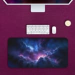 Infidu Space Desk Pad features a nebula with rich purples, blues, and pinks, set against a field of stars and cosmic clouds. Desk Pad with Keyboard and Mouse in pink background