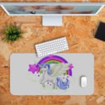 Unicorn Desk Mat with white background, rainbow, and purple stars, and a unicorn with a greenhorn surrounded by clouds.Desk Pad with Design Kept on a computer table