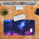 Infidu Space Desk Pad features a vivid, colorful nebula with swirling clouds of gas and dust in blue, pink, purple, and orange hues. Desk Pad with Keyboard and Mouse in orange background