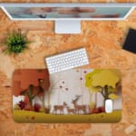 Infidu Explore Nature Desk Mat features a colorful nature scene with deer, autumn-colored trees, and falling leaves in yellow and red tones. Desk Pad kept on a plain orange background