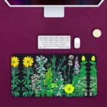 Black desk mat with colorful flower and plant illustrations, including yellow daisies and green plants, featuring a unique design. Desk Pad on the computer table