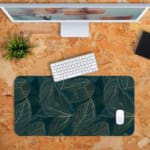 Green desk mat with outlined leaf patterns in yellow and green, featuring a unique and creative design by digital artists. Desk Mat with a computer