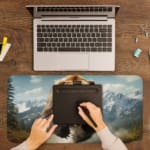 Roaring brown bear with a mountain and sky background on a desk pad, featuring cool blue skies and snow-covered mountains. A writing pad on top of the desk pad