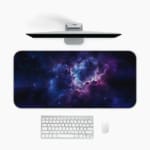 Infidu Space Desk Pad features a nebula scene with rich purples, blues, and a splash of pink, surrounded by stars and cosmic clouds. Desk Mat with a computer