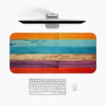 Desk pad with a vibrant striped wood texture design featuring bold colors like orange, light blue, beige, purple, and red. A desk pad under the computer