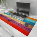 Desk pad with a vibrant striped wood texture design featuring bold colors like orange, light blue, beige, purple, and red. the desk pad is kept on the laptop