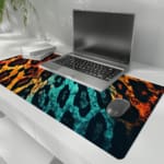 Infidu Vibrant Leopard Print Desk Pad featuring a brown and yellow leopard pattern transitioning to blue and black. the desk pad is kept on the laptop