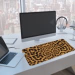 Infidu Light Beige Desk Pad with dark brown leopard print spots. A computer and laptop are next to the desk pad