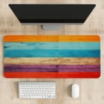 Desk pad with a vibrant striped wood texture design featuring bold colors like orange, light blue, beige, purple, and red. Desk Pad on the table