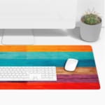 Desk pad with a vibrant striped wood texture design featuring bold colors like orange, light blue, beige, purple, and red. Desk Pad with Keyboard and Mouse on top of the desk pad