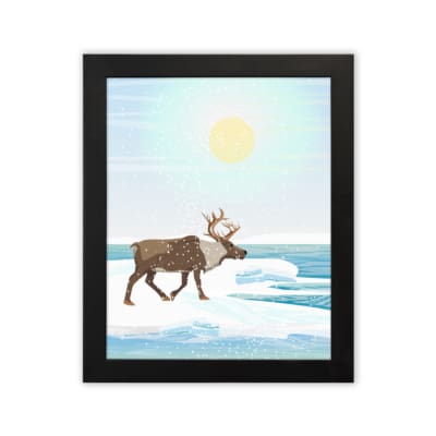 Christmas wall art featuring a reindeer walking on snow near a body of water with a bright sun and blue sky in the background. in plain white background in a black frame