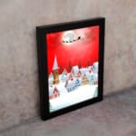 Santa Claus flying in a sleigh with reindeer against a red background, full moon, and snowy village. displayed on the wall in a black frame