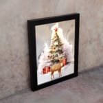 Christmas wall art featuring a white tree with red ornaments, gifts underneath, a reindeer, and a snowy background in a watercolor style. displayed on the wall in a black frame