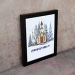 Winter scene with a small chapel, snow-covered trees, and the word CHRISTMAS below in cool colors. on the wall in a black frame