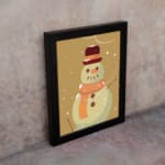 Snowman illustration with a red hat and orange scarf, framed in black, with snowflakes on a light beige background. on the wall in a black frame