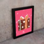 Infidu Gift Box Art - Festive Design with Snowflakes and Ribbon with brown polka dot gift box, pink background, and black frame. on the wall in a black frame