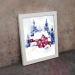 Christmas wall art featuring a pink house and blue pine trees in a watercolor style with a light background. on the wall in a white frame