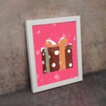 Infidu Gift Box Art - Festive Design with Snowflakes and Ribbon with brown polka dot gift box, pink background, and black frame. on the wall in a white frame