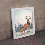 Winter-themed wall art with a reddish-brown deer, blue trees, and a light, snowy background in a watercolor style. on the wall in a white frame