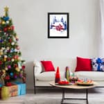 Christmas wall art featuring a pink house and blue pine trees in a watercolor style with a light background. displayed on the wall in a black frame