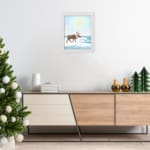 Christmas wall art featuring a reindeer walking on snow near a body of water with a bright sun and blue sky in the background. displayed on the wall in a white frame