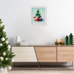 Watercolor Christmas tree painting with green, blue, and red colors, topped with a yellow star, framed in black. displayed on the wall in a white frame