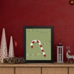 Candy cane with red and white stripes, surrounded by colorful Christmas lights on a light grey or muted green background. displayed on the table in a black frame