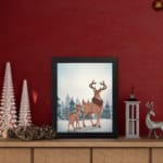 Winter-themed wall art with a reddish-brown deer, blue trees, and a light, snowy background in a watercolor style. displayed on the table in a black frame