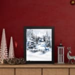 Infidu A Joyous Holiday Wall Art - Tranquil Winter Forest Scene with Deer shows a snowy forest with evergreen trees, a blue house, and a deer. on the table in a black frame