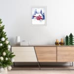 Christmas wall art featuring a pink house and blue pine trees in a watercolor style with a light background. displayed on the wall in a white frame