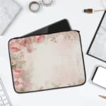 Soft beige laptop sleeve with delicate floral design in pink, green, and purple, featuring a zip closure for secure storage. laptop sleeve kept on a plain white background