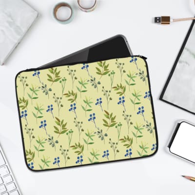 The laptop sleeve is light yellow with a floral pattern of green leaves and blue flowers. laptop sleeve kept on a plain white background